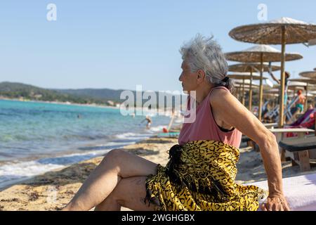 vieille dame assise sur la plage profitant de ses vacances Banque D'Images