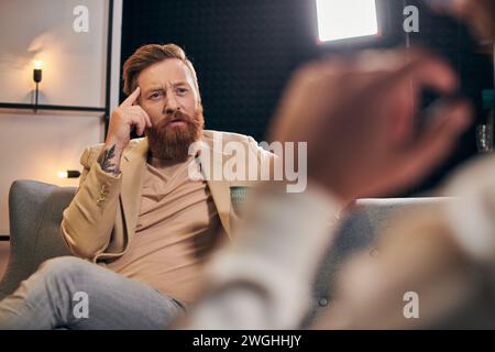 beau homme barbu avec les cheveux roux dans des vêtements élégants assis à côté de son intervieweur dans le studio Banque D'Images