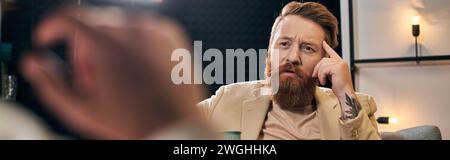 beau homme barbu avec les cheveux roux dans des vêtements élégants assis à côté de son intervieweur, bannière Banque D'Images