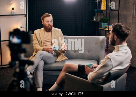 bel homme barbu avec les cheveux roux dans des vêtements élégants assis à côté de son intervieweur dans le studio Banque D'Images