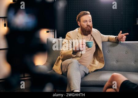 bel homme barbu avec les cheveux roux dans des vêtements élégants assis à côté de son intervieweur dans le studio Banque D'Images