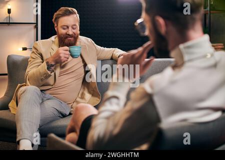 homme barbu joyeux avec les cheveux roux dans des vêtements élégants assis à côté de son intervieweur dans le studio Banque D'Images