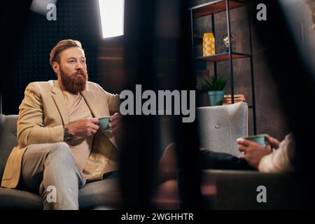 bel homme barbu avec les cheveux roux dans des vêtements élégants assis à côté de son intervieweur dans le studio Banque D'Images