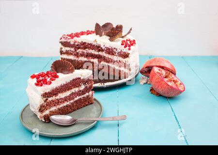 Gâteau de velours rouge aux graines de grenade, tranché sur une plaque en céramique, sur une table de planches en bois bleu Banque D'Images