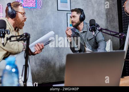 beaux hommes élégants avec barbe et écouteurs discutant des questions en studio pendant le podcast Banque D'Images