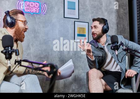 intervieweur attrayant avec les cheveux roux et son invité avec des écouteurs discutant des questions, podcast Banque D'Images