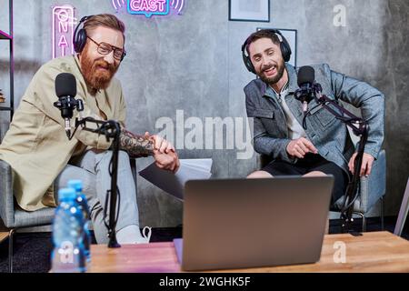 beaux hommes élégants avec barbe et écouteurs discutant des questions en studio pendant le podcast Banque D'Images