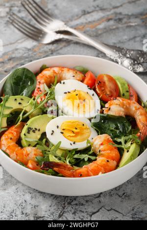 Salade diète avec crevettes tigrées, avocat, roquette, épinards, tomates et graines de sésame gros plan dans un bol sur la table. Vertical Banque D'Images