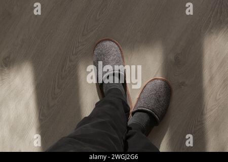 Homme portant des pantoufles de maison grises et debout sur un plancher de bois franc dans l'appartement Banque D'Images