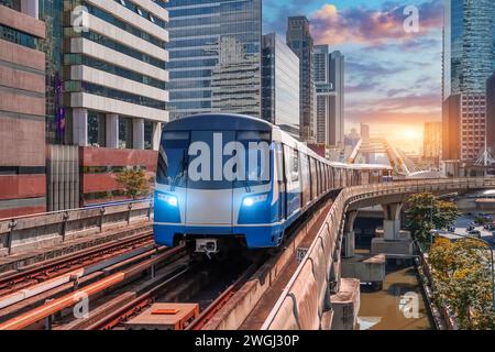 Train électrique lumineux le wagon de chemin de fer lumineux se précipite le long de la route dans le viaduc de chemin de fer de ciel de coucher de soleil parmi la ville moderne des bâtiments, SK Banque D'Images