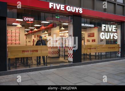 Extérieur du restaurant Five Guys Hamburger. Un homme solitaire se tient à l'intérieur regardant par la fenêtre. Bishopsgate Londres Angleterre Royaume-Uni Banque D'Images