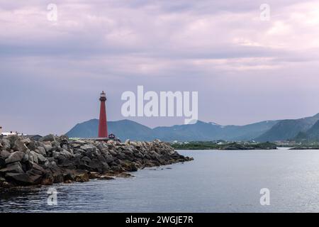 Une vue sereine sur le phare d'Andenes debout haut avec sa teinte rouge vibrante sur fond d'eaux de mer calmes, rivage rocheux et mountai lointain Banque D'Images