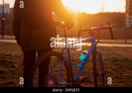 Jeune homme tenant son vélo de route et profitant d'un beau coucher de soleil. Banque D'Images