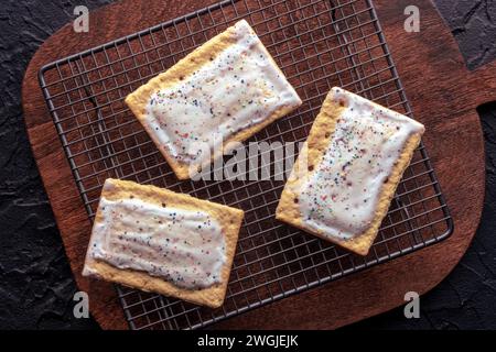 Sauter les tartes sur une grille de cuisson. Pâte grille-pain Poptart avec glaçage sur une planche à découper en bois, tir à plat suspendu Banque D'Images