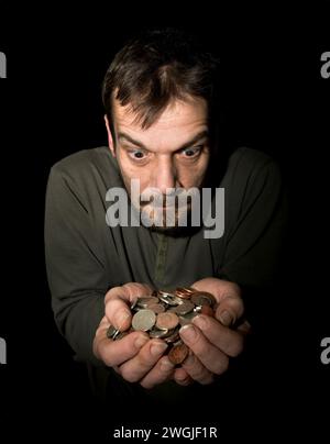 Homme caucasien (42 ans) avec les mains tendues pleines de monnaie lâche dans la monnaie sterling avec un regard avide sur le visage Banque D'Images