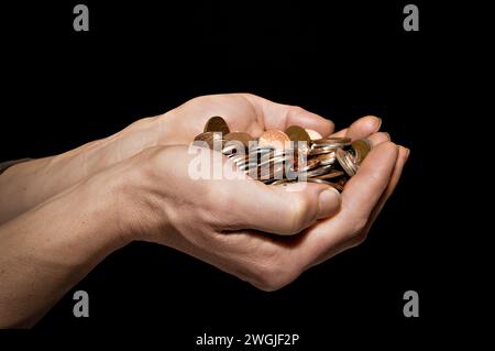 Homme caucasien (42 ans) avec les mains tendues pleines d'argent sur un fond noir Banque D'Images