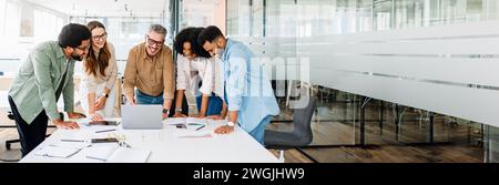 L'équipe diversifiée de professionnels s'engage dans un échange dynamique d'idées, avec des ordinateurs portables ouverts suggérant une séance de travail collaborative. Une équipe productive et coopérative lors d’un brainstorming créatif. Banque D'Images