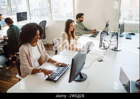 Dans un environnement de co-working spacieux et bien éclairé, un groupe diversifié de jeunes professionnels sont engagés dans leurs tâches respectives sur les ordinateurs, créant une atmosphère de productivité concentrée Banque D'Images