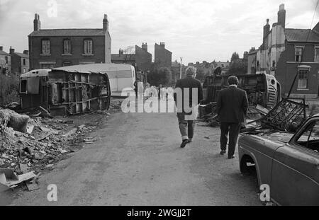 Campement de voyageurs irlandais gitans et décharge temporaire de voitures à la ferraille dans une décharge de Balsall Heath dans les années 1960 au Royaume-Uni. Balsall Heath était un quartier de bidonville. La rue vers laquelle les hommes gitans marchent est Wenman Street. Ce bricoleur a fait sa vie en collectant de la ferraille ainsi que la décharge de voiture. Le camp est l'endroit où Gosforth et Knutsford Street sont. Balsall Heath, Birmingham, Angleterre mars 1968. HOMER SYKES Banque D'Images