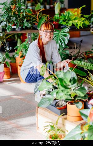 Jardiniers s'occupant de plantes. Femme jardinier arrosant la plante d'intérieur en pot dans la serre entourée de plantes et de pots, en utilisant l'arrosage blanc peut m Banque D'Images