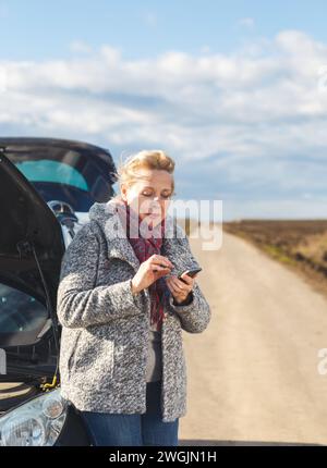 Femme âgée sur la route ayant une panne de moteur, elle appelle à l'aide. Banque D'Images