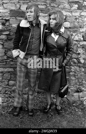 Mode britannique des années 1970. Jeune couple Margaret et Barry Kirkbride, il est habillé à la mode dans un pantalon tartan qui a été rendu populaire par le boys band The Bay City Rollers. Les cheveux longs, les longs trench-coat en cuir et les blousons bombardiers faisaient rage. Workington, Cumbria. 1975 Angleterre HOMER SYKES Banque D'Images