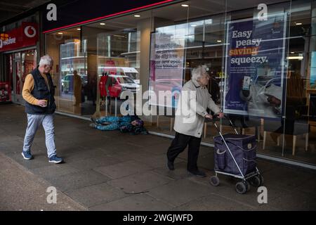 Des piétons passent devant un sans-abri alors qu'il est allongé sur le trottoir de Victoria Street dans le centre de Londres, Angleterre, Royaume-Uni Banque D'Images