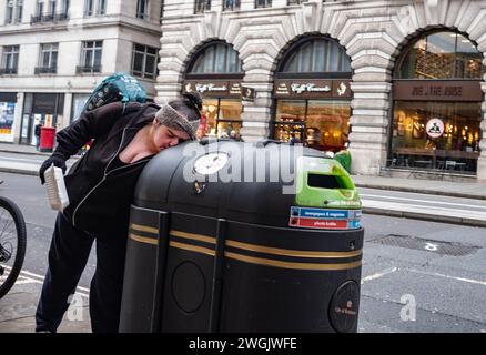 Personne sans-abri «bac plongeant» pour leurs jours de nourriture à l'intérieur d'un bac de recyclage public situé sur le trottoir le long de Piccadilly, Mayfair, Londres, Angleterre, Royaume-Uni Banque D'Images