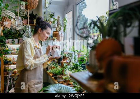 Vue latérale de la femme de beauté entrepreneur américain tenant pot de plante dans le jardin intérieur. Smiley visage jardinier portant tablier dans le magasin de plantes. Les petites entreprises Banque D'Images
