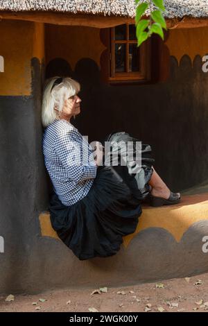 femme âgée blonde mode devant une maison africaine traditionnelle avec toit de chaume Banque D'Images