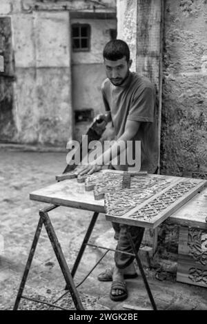 Un menuisier artisan fabriquant des panneaux de menuiserie sur une rue de la médina à Fès. Fès, la deuxième plus grande ville du Maroc, est souvent considérée comme la capitale culturelle du pays. Il est principalement connu pour sa médina fortifiée de Fès El Bali, avec son architecture médiévale marinide, ses souks animés et son atmosphère d'antan. La médina abrite des écoles religieuses telles que Bou Inania et Al Attarine, datant du XIVe siècle, toutes deux décorées de sculptures en cèdre élaborées et de tuiles ornées. Maroc. Banque D'Images