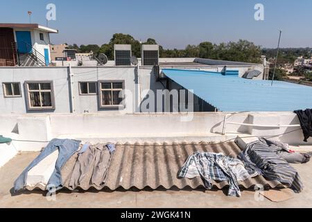 Hassan, Karnataka, Inde - 10 janvier 2023 : des vêtements colorés et des articles ménagers sont suspendus sur un toit, créant un visuel vibrant contre un b clair Banque D'Images
