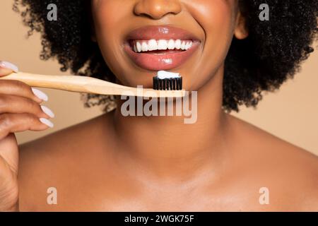 Gros plan de femme noire souriante avec brosse à dents en bambou et pâte, fond beige Banque D'Images