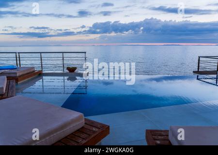 Fantastique villa sur l'eau, vue sur la terrasse avec chaises longues sous parasol, hôtel de luxe avec piscine avec vue imprenable sur l'océan. Beau spa ou bien-être co Banque D'Images