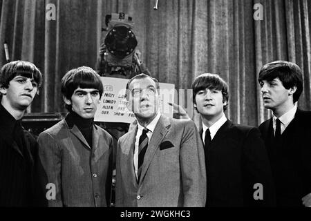 Les Beatles et Ed Sullivan posent devant une caméra de CBS et une carte de repérage énumérant les invités de Sullivan pour le spectacle de la semaine suivante qui sera diffusé à l'hôtel Deauville à Miami Beach. Après-midi, séance photo, samedi 8 février 1964 CBS' The Ed Sullivan Show CBS Studio 50, Broadway and West 53rd Street, New York, NY. De gauche à droite : Ringo Starr, George Harrison, Ed Sullivan, John Lennon, Paul McCartney Banque D'Images