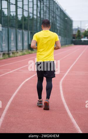 Homme actif dans les jogging de vêtements d'activité le long de la piste du stade, vue arrière de style de vie sain et actif Banque D'Images