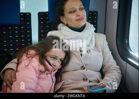 Jeune femme, mère heureuse embrassant sa petite fille, voyageant ensemble dans un train urbain confortable, regardant par la fenêtre du train de passagers, profitez Banque D'Images