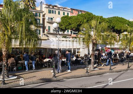 Les gens aux restaurants en plein air sur la promenade de la ville côtière pendant les vacances d'hiver, Sanremo, Imperia, Ligurie, Italie Banque D'Images