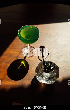 boisson d'absinthe verte dans un verre coupé sur une table en bois avec fleur de tulipe en papier dans un vase Banque D'Images