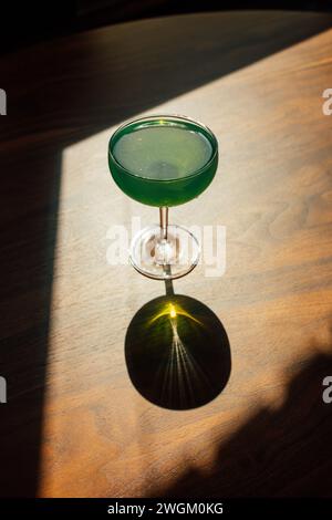 boisson d'absinthe verte dans un verre coupé avec sur une table en bois à l'intérieur au soleil avec une ombre dure Banque D'Images