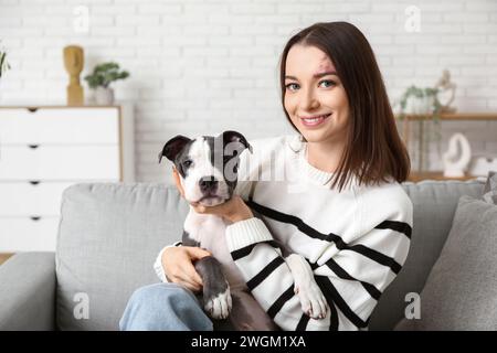 Belle jeune femme avec chiot terrier staffordshire mignon assis sur le canapé à la maison Banque D'Images