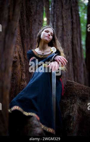 Jeune femme avec Broadsword assis assis Redwood Trees Crown Princess robes Banque D'Images
