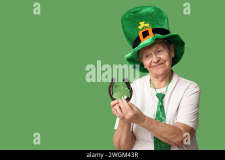 Femme senior en chapeau de leprechaun avec fer à cheval et trèfle sur fond vert. Prog Célébration de la fête de Patrick Banque D'Images