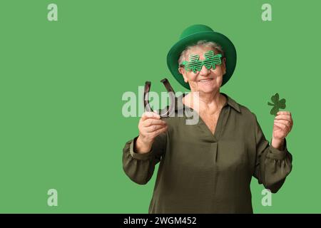 Femme senior en chapeau de leprechaun avec fer à cheval et trèfle sur fond vert. Prog Célébration de la fête de Patrick Banque D'Images