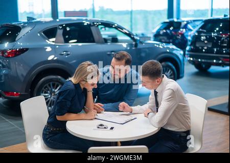 Un couple caucasien heureux signe un contrat pour l'achat d'un salon de voiture. Banque D'Images