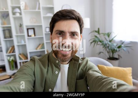 Vue à la première personne d'un homme caucasien heureux en chemise enregistrant la vidéo sur un appareil photo numérique. Influenceur populaire produisant du contenu pour un nouveau post dans social Median et un nouveau post dans un blog personnel de la maison. Banque D'Images