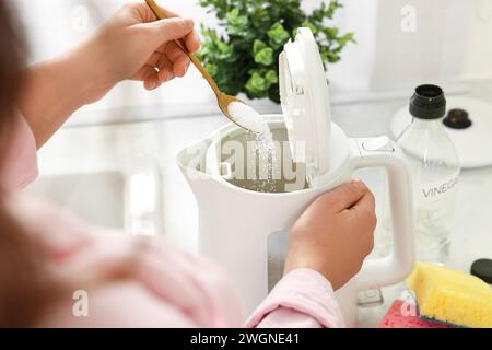 Femme ajoutant du bicarbonate de soude dans une bouilloire électrique dans la cuisine, closeup Banque D'Images