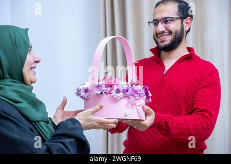 Comme surprise dans leur maison, un homme musulman heureux donne des roses à sa mère Banque D'Images