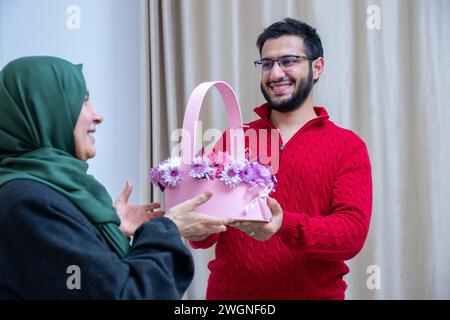 Comme surprise dans leur maison, un homme musulman heureux donne des roses à sa mère Banque D'Images