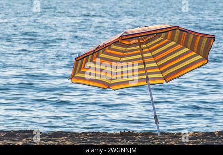Parasol rayé près d'une serviette sur une plage. Parasol de plage par une journée ensoleillée. Parapluie de protection solaire. Personne, espace de copie pour le texte, photo de voyage Banque D'Images